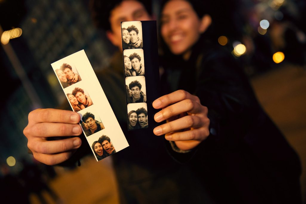 Fototessere A couple holds photo booth strips featuring black-and-white pictures of themselves.