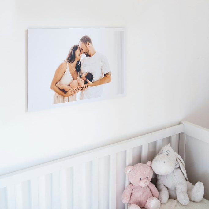 Foto Arredo Una coppia tenera abbraccia un neonato, con peluche in un lettino bianco sullo sfondo.