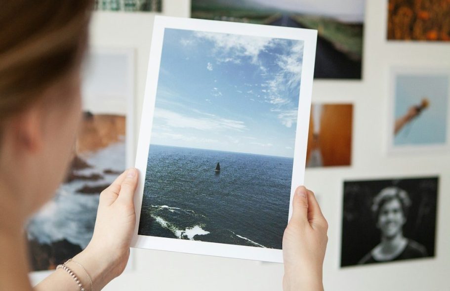 Person holding a printed photo of the ocean under a clear blue sky.