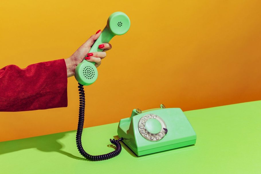 Mano che tiene un telefono verde su sfondo arancione e superficie verde.